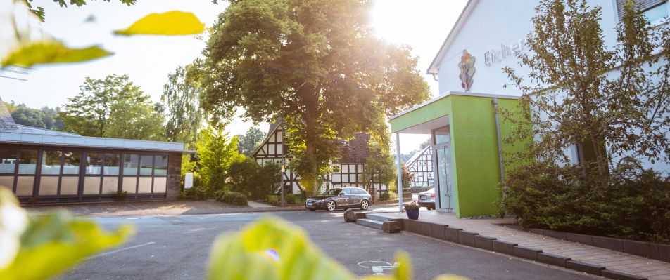 Eine sonnige Straße mit modernen und traditionellen Gebäuden, darunter das markante grüne Vordach der Eichenklinik im Eingangsbereich.