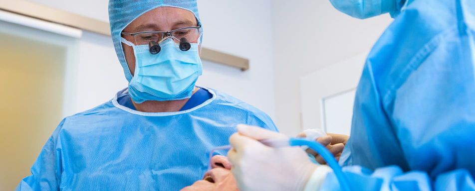 Zwei Personen in blauer OP-Kleidung führen eine zahnmedizinische Behandlung durch.