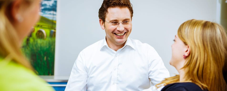 Ein lächelnder Zahnarzt beruhigt eine Frau während einer Konsultation, um ihre Zahnbehandlungsangst zu lindern.