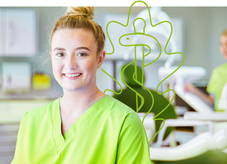 Eine Frau in grünem Kasack steht in einer Praxisumgebung. Im Hintergrund befindet sich das grüne Eichenklinik Logo und eine weitere Person sowie medizinisches Equipment zu sehen.