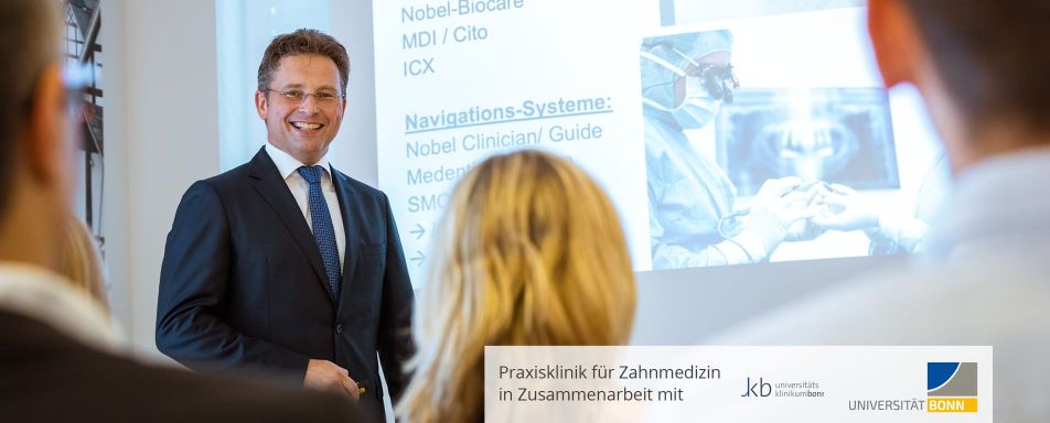 Ein Mann im Anzug hält eine Präsentation über Implantat- und Navigationssysteme in der Eichenklinik vor einem interessierten Publikum.